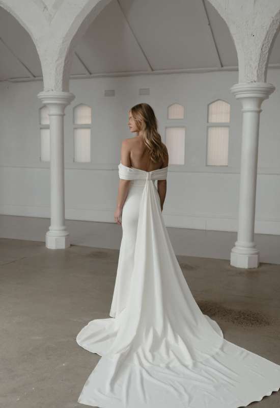 Soren by Madi Lane Bridals. Clean off the shoulder style wedding dress with detachable train at love it at stellas bridal shop in Westminster MD