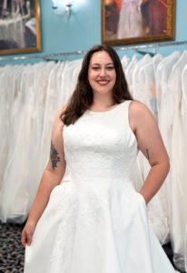 An a-line wedding dress in matte satin, featuring floral lace and a high neckline. Shown in Ivory and designed by Stella's Collection. A modern bridal gown available at Stella’s Bridal in Westminster, Maryland.