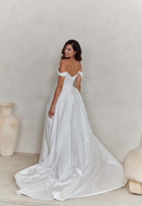 Cassidy - Stella's Bridal An a-line wedding dress in satin, featuring a basque waitline and off-the-shoulder sleeves. Shown in Ivory and designed by Serene by Madi Lane Bridal. A modern bridal gown available at Stella’s Bridal in Westminster, Maryland. Serene by Madi Lane Bridal Style SR2453 Cassidy.