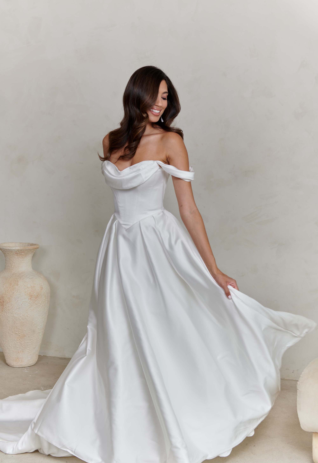 Cassidy - Stella's Bridal An a-line wedding dress in satin, featuring a basque waitline and off-the-shoulder sleeves. Shown in Ivory and designed by Serene by Madi Lane Bridal. A modern bridal gown available at Stella’s Bridal in Westminster, Maryland. Serene by Madi Lane Bridal Style SR2453 Cassidy.