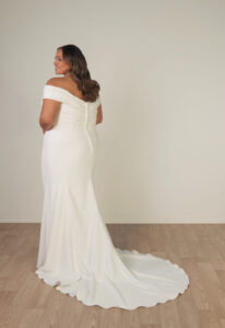 Nelly - Stella's Bridal Stella York SY8330 wedding dress featuring a fitted silhouette with off-the-shoulder neckline, crepe skirt, and ruched details. Available at Stella’s Bridal in Westminster, Maryland.