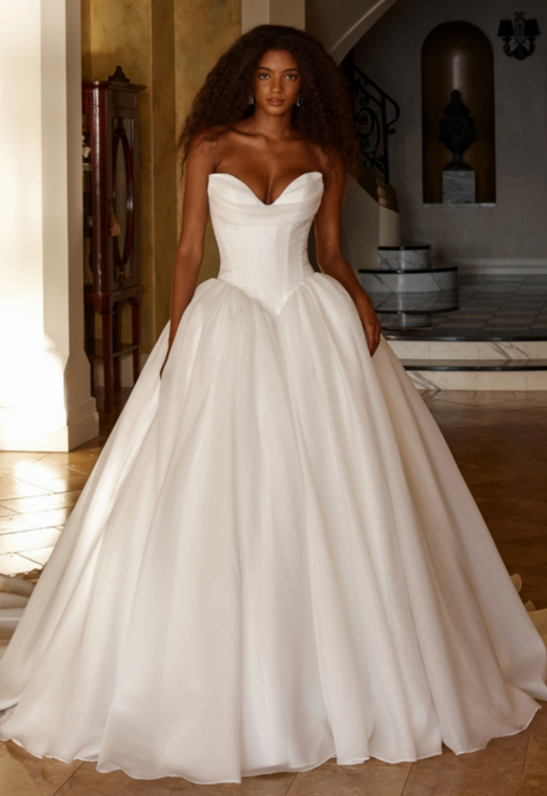 Opera - Stella's Bridal Madi Lane Opera wedding dress featuring a ballgown silhouette with cat-eye neckline, organza skirt, and corseted details. Available at Stella’s Bridal in Westminster, Maryland.