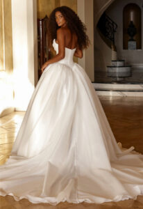 Opera - Stella's Bridal Madi Lane Opera wedding dress featuring a ballgown silhouette with cat-eye neckline, organza skirt, and corseted details. Available at Stella’s Bridal in Westminster, Maryland.
