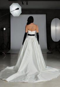 Evie Young O'Hara wedding dress featuring a fitted drop waist silhouette with straight neckline, black accent, and ruched details. Available at Stella’s Bridal in Westminster, Maryland.